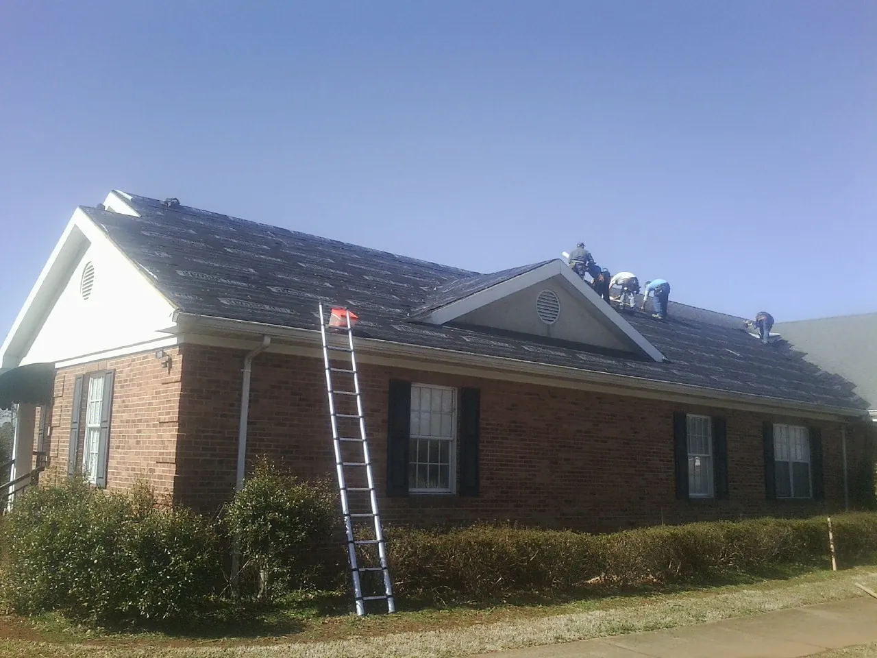 Crew tearing shingles off a brick ranch roof with a ladder set — Metal Roof Repair work by our crew in North Street