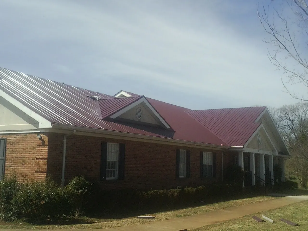 Red metal roof with gabled entries on a long brick building, from a Hail Damage Roof Repair job in North Street