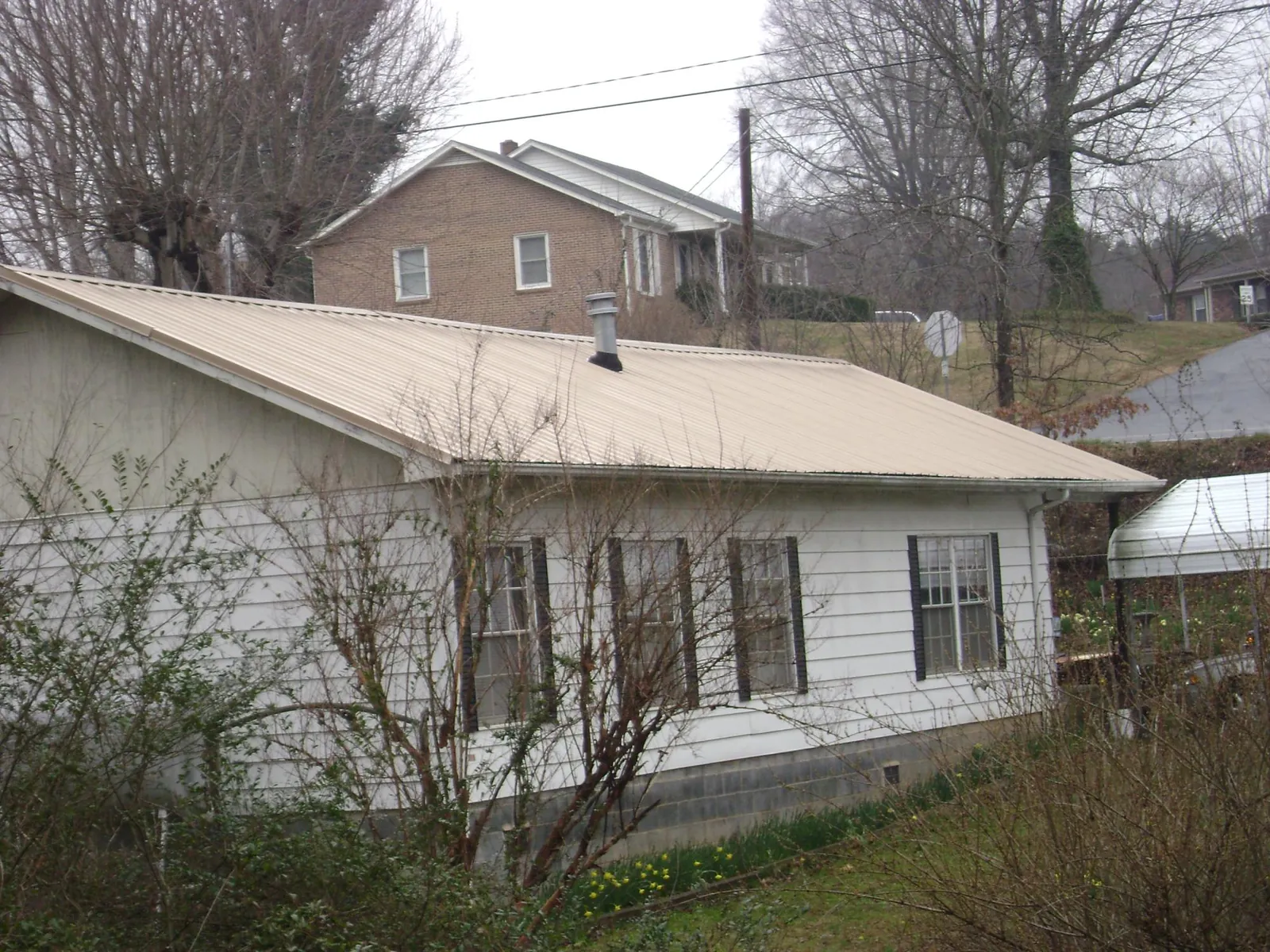 Tan metal roof on a white sided house set into a hillside — Commercial Roofing by Roofing Brothers in North Street